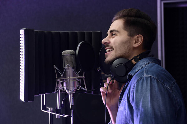 Молодой певец с песней для микрофона в студии
