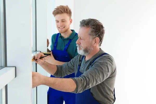 Service men measuring window for installation indoors