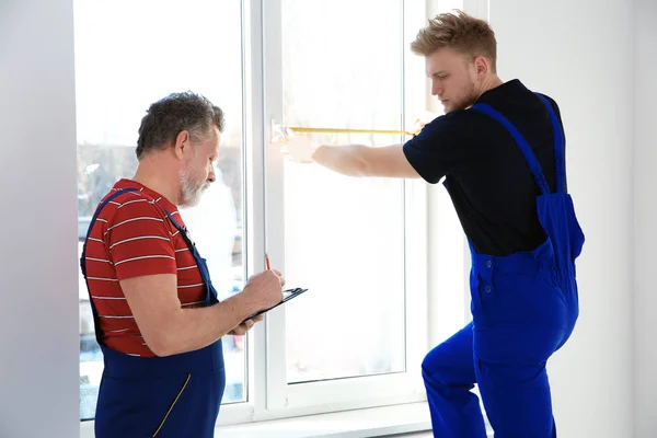 Service men measuring window for installation indoors