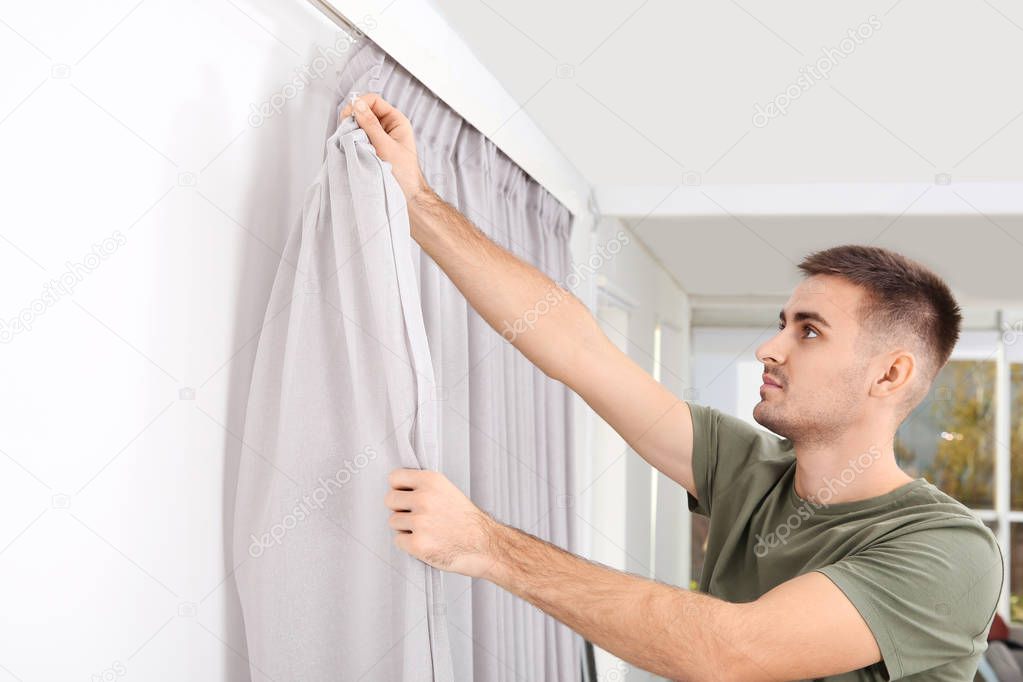 Man hanging window curtain indoors. Interior decor element