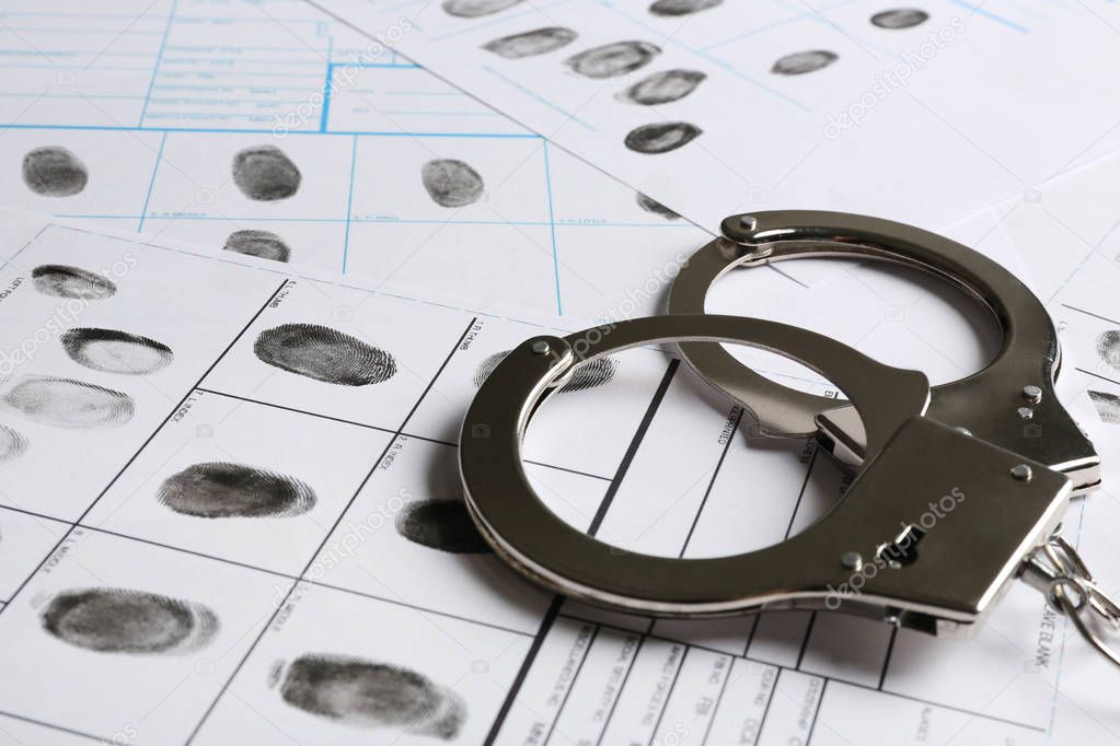 Handcuffs and fingerprint record sheets, closeup. Criminal investigation