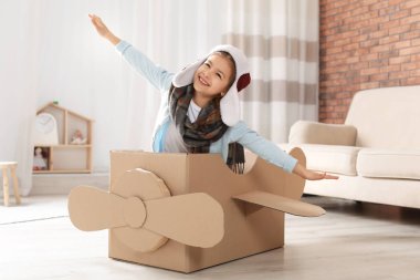 Oturma odasında karton uçak ile oynayan sevimli küçük kız