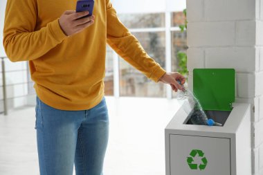 Genç adam bin ve metal kapalı, closeup boş plastik şişe atma. Atık geri dönüşüm