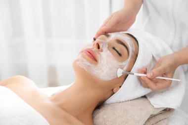 Spa salonu müşterinin yüzüne maske uygulayarak güzellik uzmanı