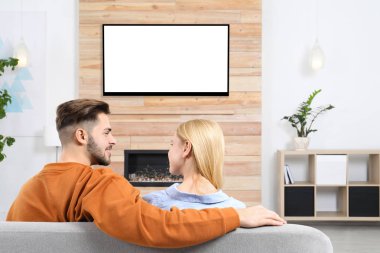 Oturma odasındaki kanepede televizyon izleyen çift.