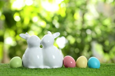 Sevimli seramik Easter bunnies ve bulanık arka plan, metin için yer yeşil çimenlerin üzerinde boyalı yumurta