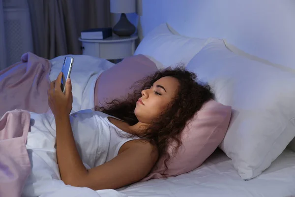 晚上带着手机的年轻非洲裔美国妇女。睡觉 — 图库照片
