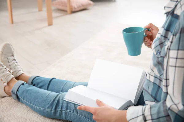 Hermosa mujer joven con taza de libro de lectura de café en el suelo en casa — Foto de Stock