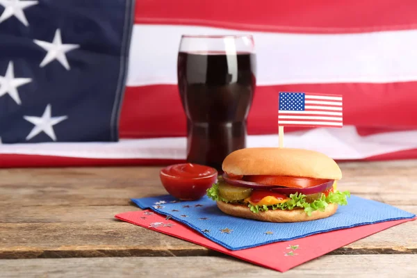 Burger with USA flag, drink and sauce on wooden table, space for text. Traditional American food