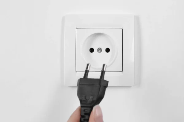 Mujer poniendo enchufe en toma de corriente sobre fondo blanco, primer plano. Equipos de electricista — Foto de Stock