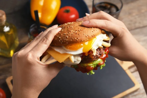 Žena držící chutné burger se sázeným vejcem nad stůl, closeup — Stock fotografie
