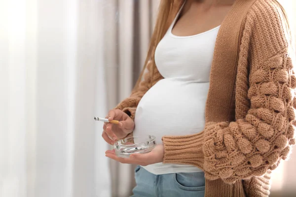 Молодая беременная женщина курит дома, крупным планом. Вред нерожденному ребенку — стоковое фото