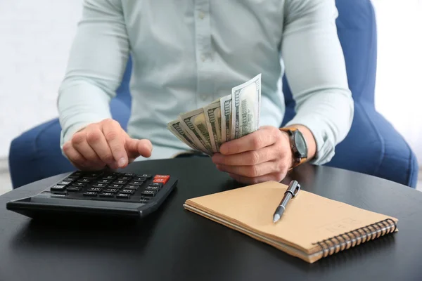 Zakenman met geld, rekenmachine en notebook aan tafel tegen lichte achtergrond, close-up — Stockfoto