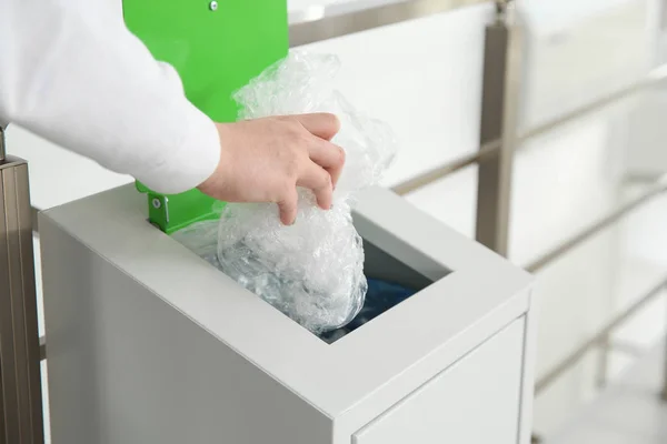 Mujer joven lanzando película de plástico en la papelera de metal en el interior, primer plano. Reciclaje de residuos — Foto de Stock