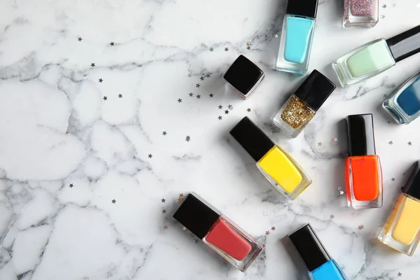 Bottles of nail polish on marble background, top view with space for text — Stock Photo, Image