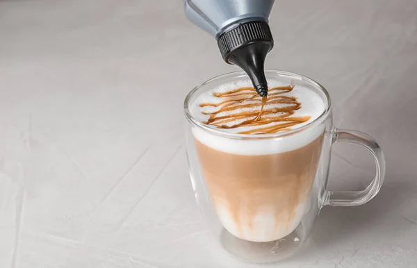 Adding caramel topping to latte macchiato on table, space for text — Stock Photo, Image