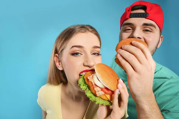 Happy couple eating burgers on color background — Stock Photo, Image