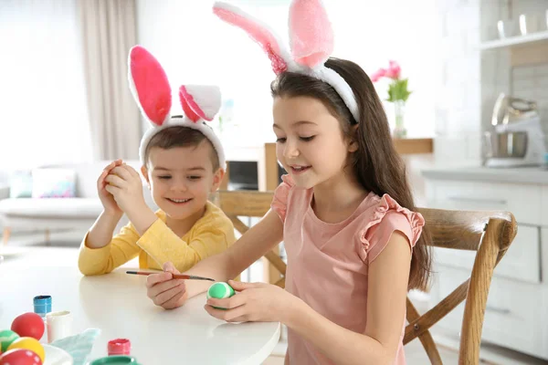 Niedliche Kinder mit Hasenohren-Stirnbändern bemalen Ostereier in der Küche — Stockfoto