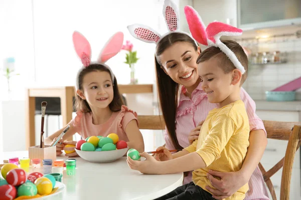 Ibu dan anak-anaknya dengan ikat kepala kelinci melukis telur Paskah di dapur — Stok Foto