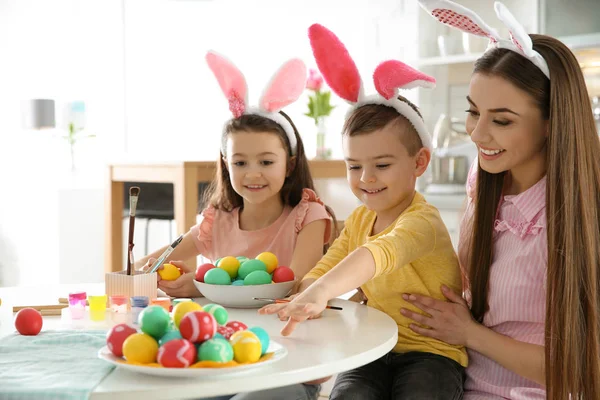 Mãe e seus filhos com orelhas de coelho headbands pintura ovos de Páscoa na cozinha, espaço para texto — Fotografia de Stock