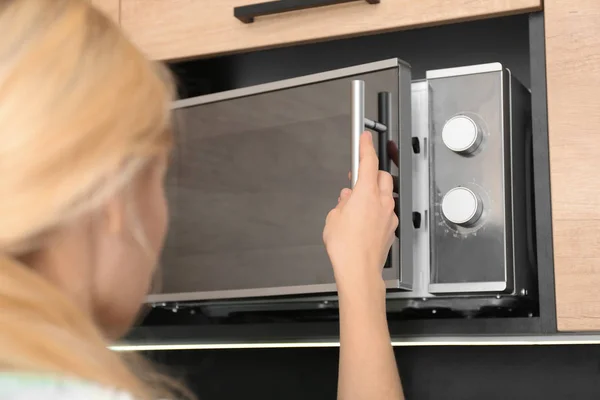 Young woman using microwave oven in kitchen, closeup