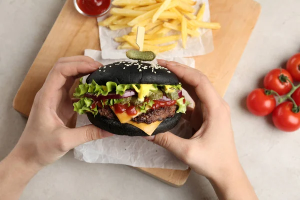 Žena držící černý burger stolu servírované, closeup — Stock fotografie