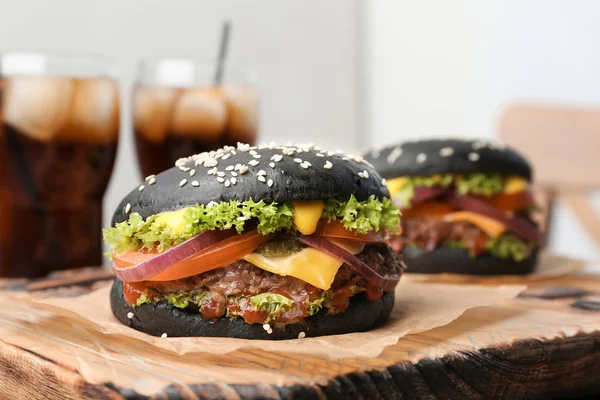 Tasty burgers with black buns on board, closeup