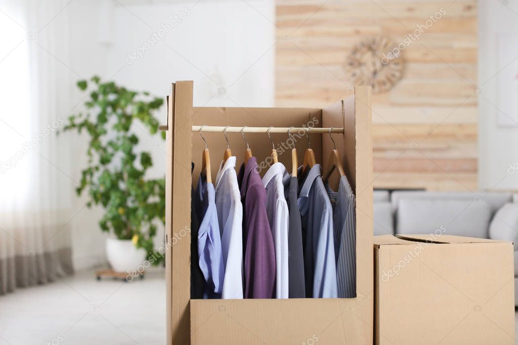 Cardboard wardrobe box with clothes on hangers in living room