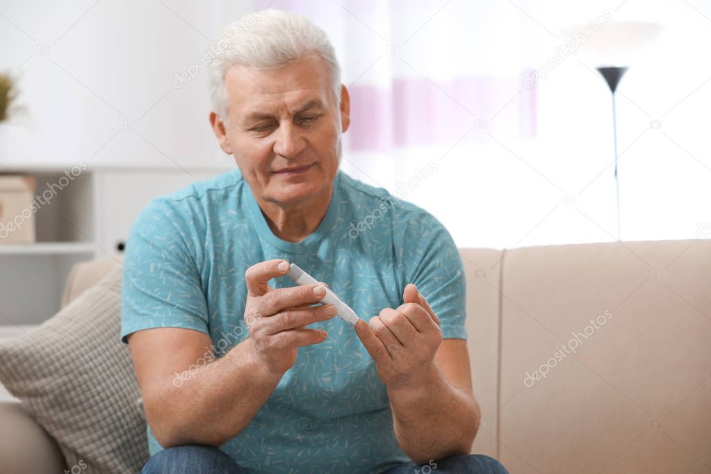 Senior man using lancet pen at home. Diabetes control