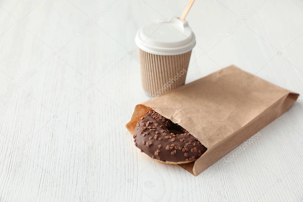 Tasty donut in paper bag and coffee on wooden table. Space for text