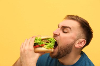 Genç adam renk arka plan üzerinde lezzetli hamburger yeme. Metin için yer