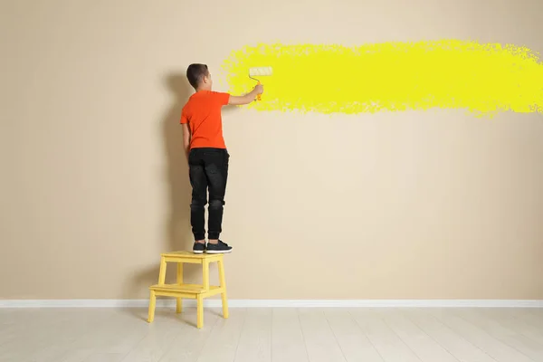 Το παιδί στην καρέκλα ζωγραφική βήμα με κυλινδρική βούρτσα στον τοίχο χρώμα — Φωτογραφία Αρχείου