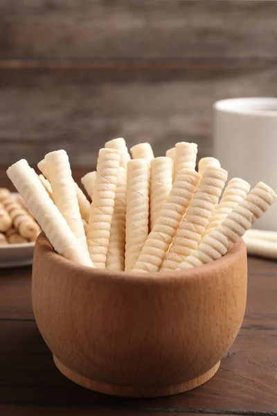 Bowl with wafer rolls on wooden table, closeup