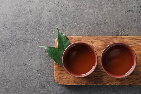 Placa com xícaras de chá oolong acabado de fazer em fundo cinza, vista superior com espaço para texto — Fotografia de Stock