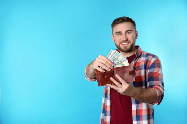 Happy young man putting money into wallet on color background. Space for text — Stock Photo, Image