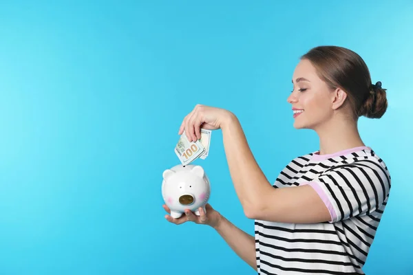 Šťastná mladá žena dát peníze do prasátko na barvu pozadí. Prostor pro text — Stock fotografie