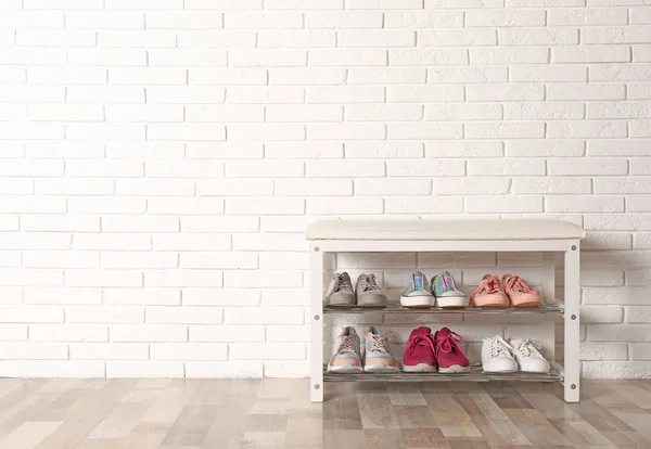 Shoe storage bench with different sneakers near brick wall, space for text