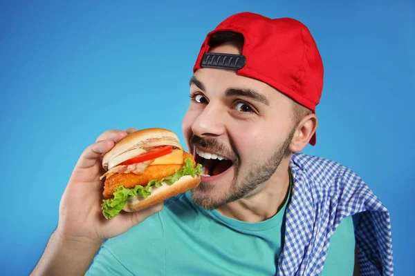 Stilig man äta välsmakande hamburgare på färgbakgrund — Stockfoto