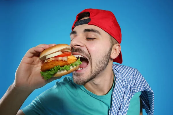 Bonito homem comendo hambúrguer saboroso no fundo da cor — Fotografia de Stock