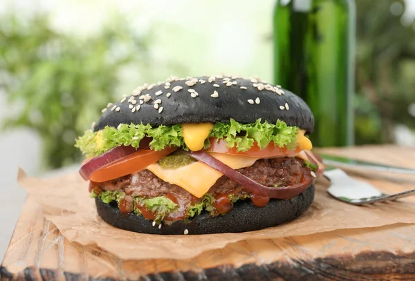Deska s černým burger na rozmazané pozadí, closeup — Stock fotografie
