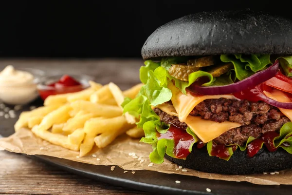 Deska s černým burger a hranolky na stole, closeup. Prostor pro text — Stock fotografie