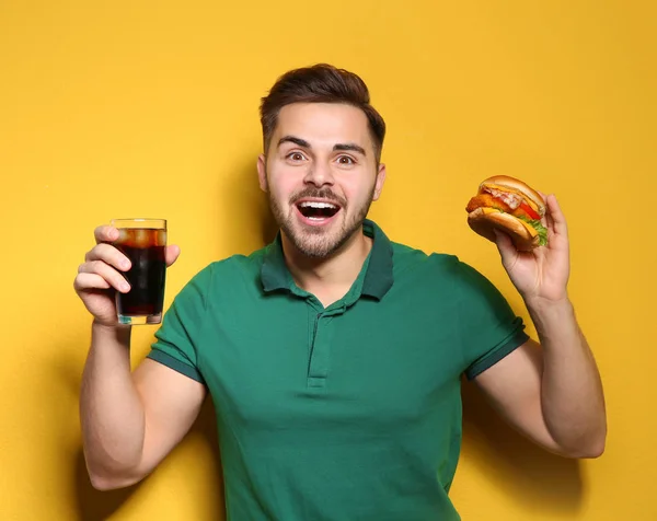 Handsome man with tasty burger and cola on color background. Space for text — Stock Photo, Image