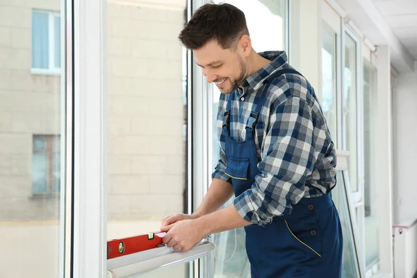 Byggnadsarbetare med vattenpass när du installerar fönster inomhus — Stockfoto