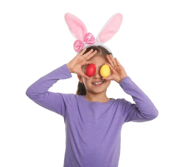Kleines Mädchen mit Hasenohren Stirnband hält Ostereier in der Nähe der Augen auf weißem Hintergrund — Stockfoto