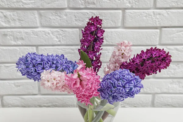 Vackra hyacinter i glasvas på bordet mot tegelvägg. Vårens blommor — Stockfoto