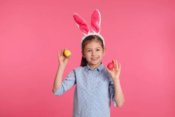 Little girl in bunny ears headband holding Easter eggs on color background — Stock Photo, Image