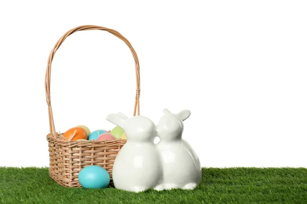 Conejitos de Pascua de cerámica y huevos teñidos sobre hierba verde sobre fondo blanco, espacio para texto —  Fotos de Stock