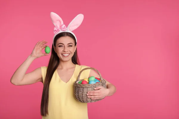 美丽的妇女在兔子耳朵头带举行篮子与复活节彩蛋在颜色背景, 文本空间 — 图库照片