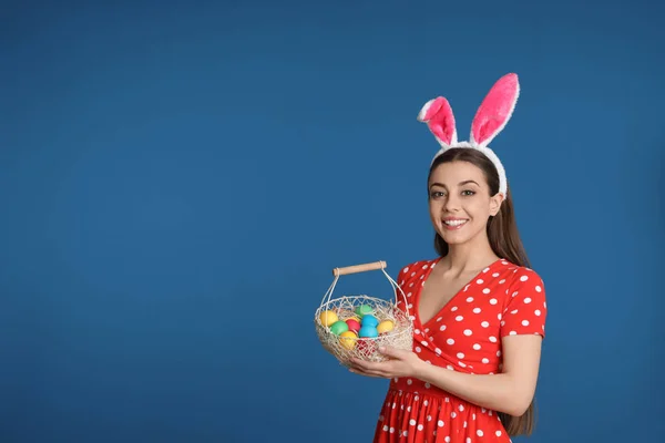 美丽的妇女在兔子耳朵头带举行篮子与复活节彩蛋在颜色背景, 文本空间 — 图库照片