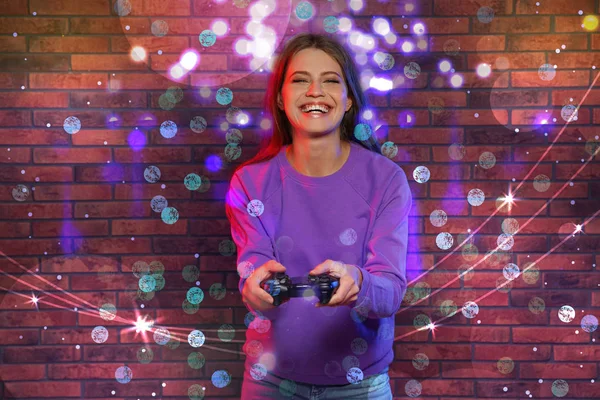 Emocional joven mujer jugando videojuegos contra la pared de ladrillo —  Fotos de Stock